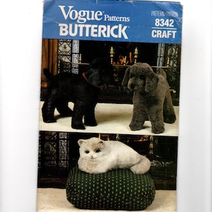 Peut inclure: Une pochette de patron de couture Vogue Patterns Butterick 8342 représentant un chien noir, un chien marron et un chat blanc allongé sur un coussin vert à motifs. L'en-tête bleu affiche le texte Vogue Patterns, BUTTERICK et 8342 CRAFT.