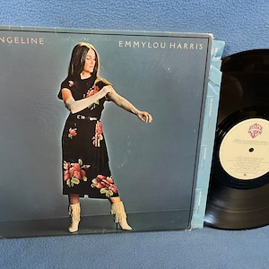 May include: A vinyl record album cover featuring a woman in a black and floral dress with white boots. The album is titled "Evangeline" by Emmylou Harris.