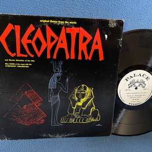 May include: A black vinyl record album cover with the title "CLEOPATRA" in red letters. The cover features a black and white illustration of an Egyptian woman and a sphinx. The album is titled "Mystic Melodies of the Nile" and features Bill Evans at the organ with the Symphony Orchestra. The record label is black with a white label that says "PALACE" in a crest.