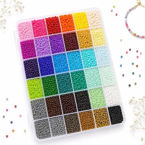 Puede incluir: Un contenedor de almacenamiento rectangular de plástico transparente lleno de pequeñas cuentas de vidrio redondas organizadas en treinta y seis compartimentos individuales. Las cuentas están clasificadas por color, con un espectro completo que incluye rosa, rojo, naranja, amarillo, azul, verde, marrón, negro y tonos metálicos.
