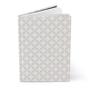 May include: A hardcover book standing upright with a light gray and white geometric pattern on the cover. The pattern consists of repeating four-petaled floral shapes with a small dot in the center of each. The pages are visible at the top.