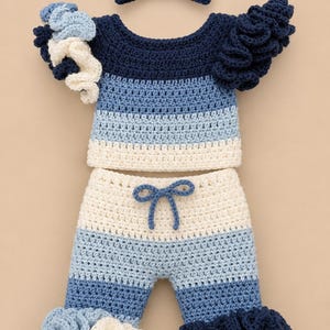 May include: A crochet set consisting of a short-sleeved top, pants, and a headband. The garments feature horizontal stripes in navy blue, light blue, and cream. The top and pants have ruffled cuffs in matching colors, and the pants include a drawstring.