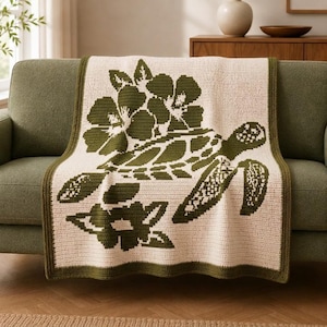 May include: A rectangular crochet blanket featuring a cream-colored base with a dark olive green pattern. The design displays a sea turtle swimming among large tropical flowers. The blanket is finished with a solid dark olive green border.