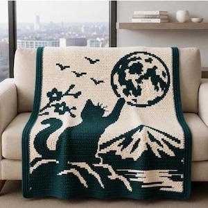 Puede incluir: Una manta de ganchillo rectangular con un diseño en verde oscuro y crema. El patrón muestra a un gato alcanzando una gran luna llena, junto a la silueta de una montaña, una rama con flores y pequeños pájaros volando.
