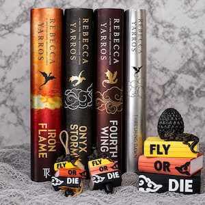 May include: Four hardcover books by Rebecca Yarros titled Iron Flame, Onyx Storm, Fourth Wing, and Threshing Dawn, accompanied by two small hanging ornaments and a stack of three miniature books with the text Fly Or Die and a dragon figure.