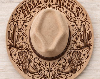 May include: A tan felt hat with a dark brown band featuring laser-engraved designs on the brim. The text HELL ON HEELS is arched at the top, flanked by steer skulls, cacti, flowers, and cowboy boots in a symmetrical arrangement.