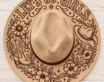 May include: A tan felt hat featuring a dark brown band and laser-engraved designs on the brim. The text LET'S GO GIRLS is arched at the top, accompanied by illustrations of a cowboy boot, a small cowboy hat, and various floral motifs.