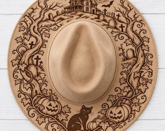 May include: A tan felt fedora hat featuring a dark brown laser-engraved design of a haunted house, a graveyard with tombstones, twisted trees, two jack-o'-lanterns, and a black cat sitting at the bottom center of the wide brim.