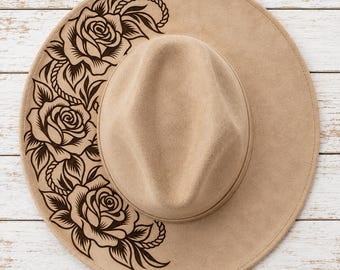 May include: A tan felt fedora hat featuring a dark brown laser-engraved floral pattern on the left side of the brim. The design consists of three blooming roses surrounded by leaves and a rope-like detail, creating a contrast against the hat.