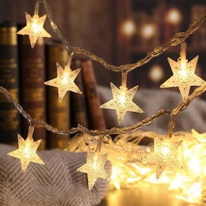 May include: A string of LED lights featuring clear, textured star-shaped covers. Each star houses a warm white light, connected by a thin, flexible wire. The lights are arranged in a draped formation, creating a glowing, illuminated display.