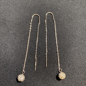 May include: A pair of silver-toned threader earrings featuring a delicate chain design. Each earring terminates in a small, spherical charm encrusted with numerous tiny, reflective clear crystals that catch the light, creating a sparkling effect.