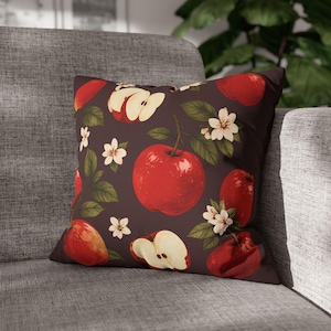 Peut inclure: Un coussin carré avec un fond marron foncé orné d'un motif répétitif de pommes rouges entières, de quartiers de pommes, de feuilles vertes et de petites fleurs blanches à cinq pétales réparties sur toute la surface.