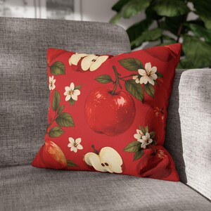 Peut inclure: Un coussin carré avec un fond rouge vif orné d'un motif répétitif de pommes rouges entières, de quartiers de pommes, de feuilles vertes et de petites fleurs blanches à cinq pétales. Le motif est réparti uniformément sur toute la surface.
