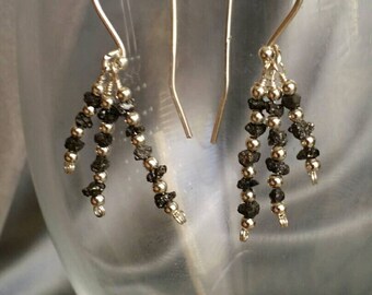 May include: A pair of silver earrings with black diamond beads. The earrings are dangle style and have a simple design.