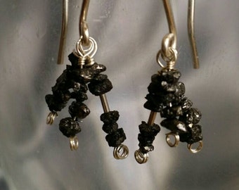 May include: A pair of silver earrings with black diamond accents. The earrings are shaped like a small cluster of diamonds.
