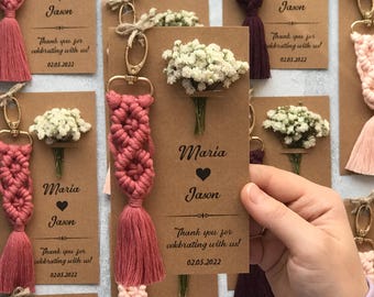 May include: Macrame keychains with gold-tone lobster clasps and attached dried white baby's breath flowers on brown cardstock tags. The tags feature the printed text Maria, Jason, and Thank you for celebrating with us, along with the date 02.05.2022.