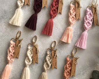May include: A collection of nine macrame keychains in various colors including cream, burgundy, dusty rose, peach, and light pink. Each keychain features a gold-tone metal clasp and a wooden tag engraved with the text "Julia & Ethan September 20, 2022".