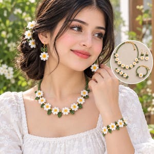Può includere: Un set di gioielli con fiori di margherita bianchi con centri gialli e foglie verdi. Il set include una collana, un braccialetto e orecchini pendenti. I fiori sono disposti in un motivo ripetuto lungo il cordino verde della collana e del braccialetto, con orecchini floreali abbinati e un accessorio per capelli.