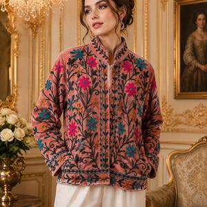 May include: A dusty rose velvet jacket featuring a mandarin collar and long sleeves. The garment is adorned with intricate floral embroidery in shades of teal, magenta, and orange, with dark green vine patterns covering the front and sleeves.