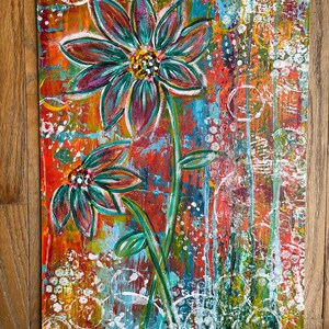 May include: A rectangular canvas painting featuring two stylized flowers with dark teal and purple petals. The background is a vibrant, textured mix of red, orange, and blue paint with white circular patterns and vertical drips throughout the composition.