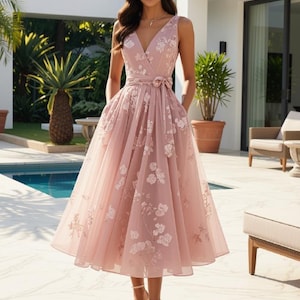 May include: A sleeveless tea-length dress in a dusty rose pink hue, featuring a V-neckline, a wrap-style bodice with a tie-waist belt, and a full, pleated skirt. The fabric is adorned with a delicate white floral pattern throughout the garment.