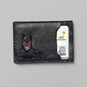 May include: A black leather card holder featuring an embossed Batman mask with a person's face visible in the cutout. The name William Garcia is engraved on the front. A driver's license with a gold star and the text Class D BOAT 05-20-2014 is inserted.