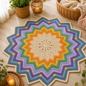 Pode incluir: Um tapete de crochê redondo em forma de estrela com um padrão de gradiente arco-íris vibrante que transita de um centro creme para laranja, amarelo, verde e azul, finalizado com uma borda roxa e pequenos detalhes de flores amarelas.