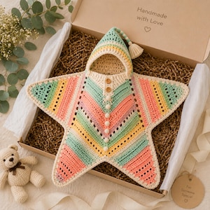 May include: A star-shaped crochet baby blanket with a hood, featuring pastel stripes in mint green, yellow, peach, and lavender. The garment includes a pointed hood with a tassel, two wooden buttons, and a row of small white pom-pom buttons down the front.