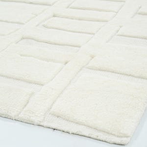 May include: A solid off-white area rug featuring a raised, textured geometric pattern of repeating rectangular blocks. The surface displays a high-pile construction with distinct depth between the elevated rectangular shapes and the flat base.