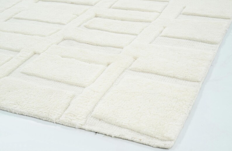 May include: A solid off-white area rug featuring a raised, textured geometric pattern of repeating rectangular blocks. The surface displays a high-pile construction with distinct depth between the elevated rectangular shapes and the flat base.
