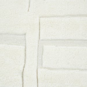 May include: A cream-coloured textile featuring a raised, tufted geometric pattern of rectangular blocks arranged in a grid-like formation. The surface displays a contrast between the thick, soft, high-pile tufted sections and the flat, woven base.