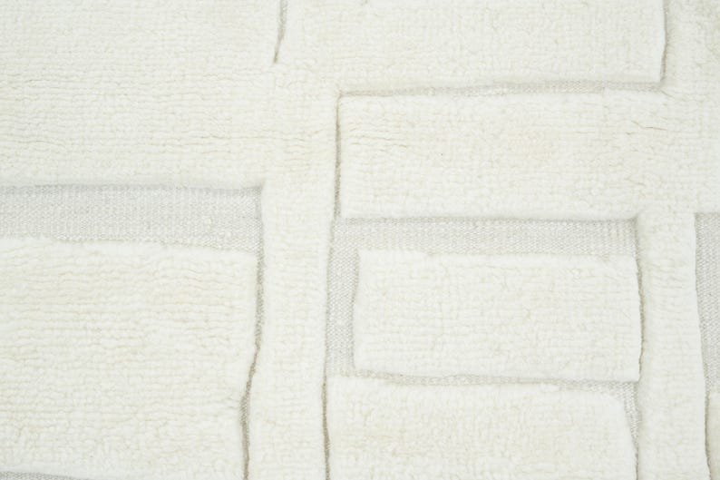 May include: A cream-coloured textile featuring a raised, tufted geometric pattern of rectangular blocks arranged in a grid-like formation. The surface displays a contrast between the thick, soft, high-pile tufted sections and the flat, woven base.