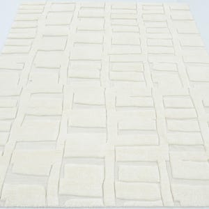 May include: A rectangular area rug in a solid off-white colour featuring a raised, textured geometric pattern of repeating rectangular blocks arranged in a grid-like formation across the entire surface of the floor covering.