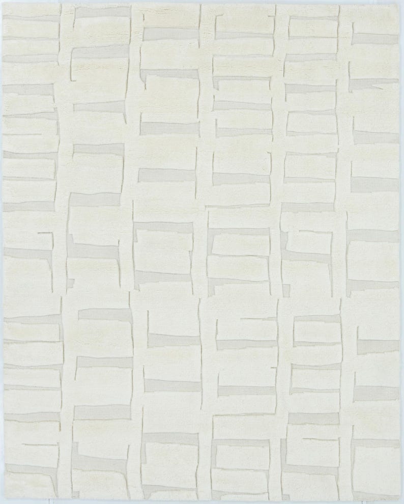 May include: A rectangular area rug in a solid off-white colour featuring a repeating geometric pattern of raised, textured rectangular blocks arranged in a grid-like formation, creating a subtle depth and dimension across the entire surface.