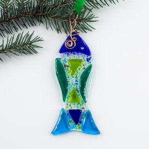 May include: A blue, green, and white glass fish ornament with a copper wire hanger. The fish is made of stained glass and has a speckled texture.