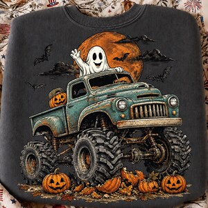 Puede incluir: Una sudadera gris carb&oacute;n con un gr&aacute;fico de un cami&oacute;n monstruo color verde azulado con neum&aacute;ticos grandes. Un fantasma blanco saluda desde la cabina, con una calabaza en la parte trasera. La escena incluye una luna naranja grande y murci&eacute;lagos.