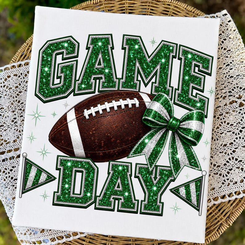 May include: A white rectangular sign featuring the text GAME DAY in large green glittery block letters. A brown football with white laces sits in the center, accompanied by a green and white glittery bow and two small pennant flags.