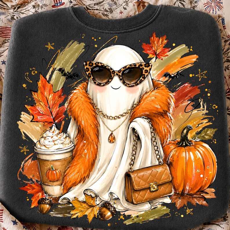 May include: A dark grey sweatshirt featuring a graphic of a white ghost wearing leopard print sunglasses, a gold chain necklace, and an orange faux fur stole. The ghost holds a quilted brown handbag next to a pumpkin, a coffee cup, and autumn leaves.