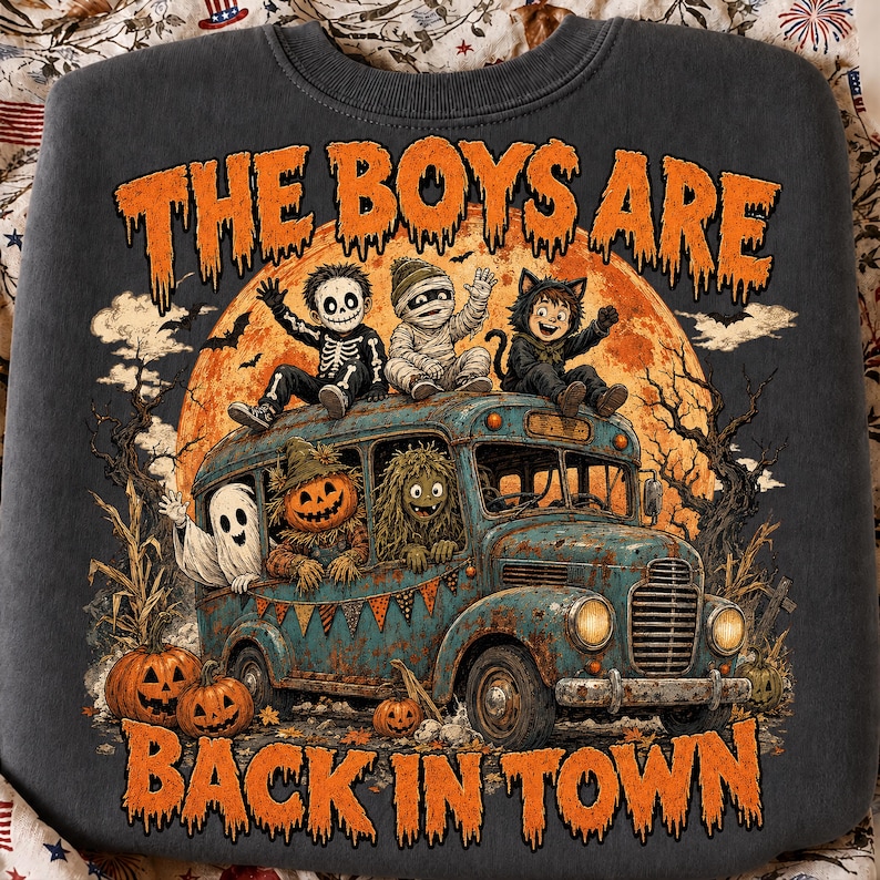 Puede incluir: Una sudadera gris carb&oacute;n con un gr&aacute;fico de un autob&uacute;s antiguo lleno de ni&ntilde;os disfrazados, incluyendo un esqueleto, momia, gato, fantasma, calabaza y monstruo. El texto THE BOYS ARE BACK IN TOWN aparece frente a una gran luna naranja.