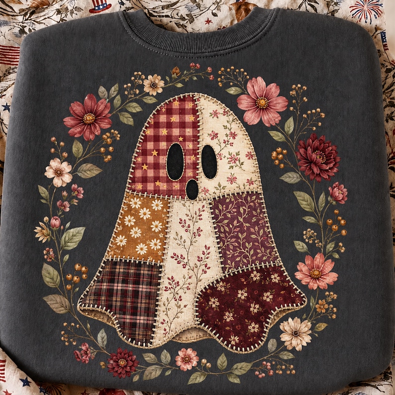 K&ouml;nnte beinhalten: Ein anthrazitfarbenes Sweatshirt mit einer zentralen Grafik eines Geistes, der aus verschiedenen Patchwork-Stoffmustern wie Karos, Blumen und Sternen zusammengesetzt ist. Der Geist ist von einem kreisf&ouml;rmigen Kranz aus Herbstblumen umgeben.
