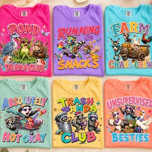 May include: Six crew neck t-shirts in bright colors featuring graphic prints of animals. The shirts display text including Pond Drama Club, Running on Snacks, Farm Chaos Crew, Absolutely Not Okay, Trash Panda Club, and Unsupervised Besties.
