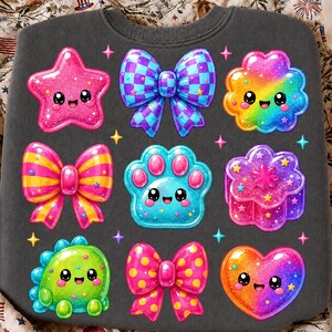 May include: A dark gray sweatshirt featuring a grid of nine colorful, glittery, and patterned icons including a pink star, a checkered bow, a rainbow flower, a striped bow, a blue paw print, a purple flower, a green dinosaur, a polka dot bow, and a heart.