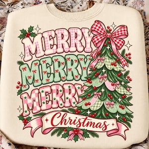 May include: A cream-colored sweatshirt featuring a graphic print with the text MERRY MERRY MERRY Christmas. The design includes a stylized green Christmas tree decorated with red berries, pink bows, and a large red and white gingham bow on top.