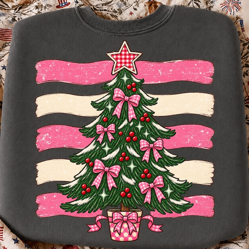 May include: A charcoal gray crewneck sweatshirt featuring a graphic of a green Christmas tree decorated with pink gingham bows, red berries, and a matching gingham star topper. The tree is set against horizontal pink and cream distressed brushstrokes.