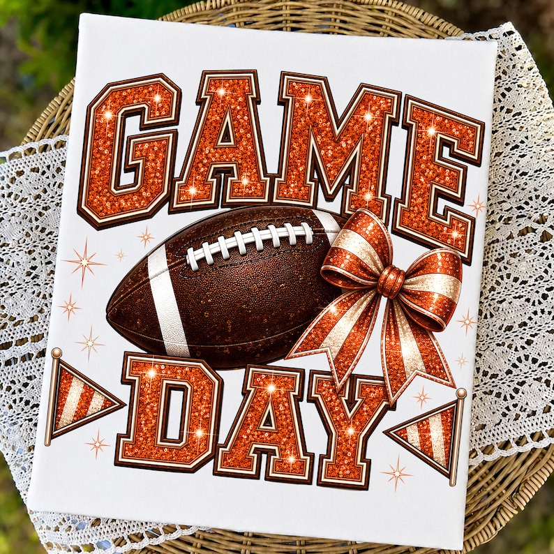 May include: A white rectangular sign featuring the text GAME DAY in large orange glitter block letters. A brown football with white laces is positioned between the words. An orange glitter bow and two small pennant flags decorate the design.