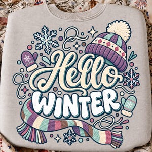 May include: A light gray crewneck sweatshirt featuring a colorful graphic print with the text Hello Winter. The design includes a purple knit hat with a white pom-pom, a striped scarf in shades of blue, purple, and tan, two mittens, and snowflakes.
