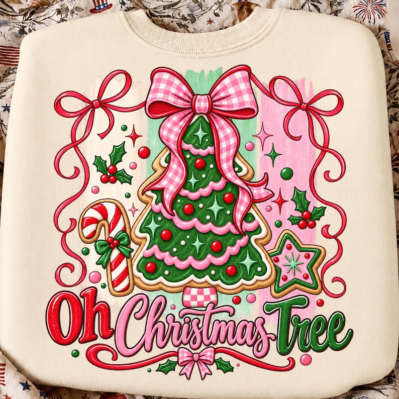 May include: A cream-colored sweatshirt featuring a graphic of a green Christmas tree shaped like a cookie with pink icing, topped with a large pink gingham bow. The design includes a candy cane, a star cookie, holly, and the text Oh Christmas Tree.