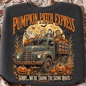 Puede incluir: Una sudadera gris oscuro con un gr&aacute;fico de un cami&oacute;n azul oxidado que transporta calabazas y ni&ntilde;os disfrazados. El texto dice PUMPKIN PATCH EXPRESS y SORRY... WE'RE TAKING THE SCENIC ROUTE. Una luna llena y murci&eacute;lagos en el fondo.