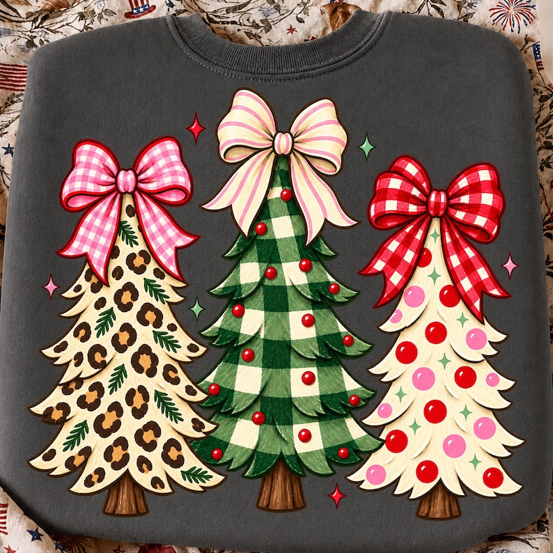 May include: A charcoal gray sweatshirt featuring a graphic of three stylized Christmas trees. The left tree has a leopard print pattern and a pink gingham bow. The center tree is green plaid with red ornaments and a striped bow. The right tree is cream with red and pink polka dots and a red gingham bow.
