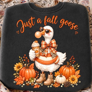 May include: A dark grey sweatshirt featuring a white goose wearing heart-shaped sunglasses, a plaid bow, and an orange sweater. The goose holds a coffee cup with a pumpkin design. The text reads Just a fall goose, surrounded by pumpkins and leaves.